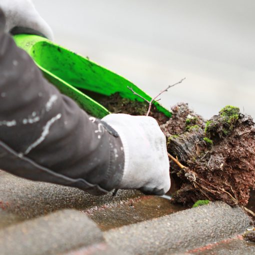 Very dirty gutter being cleared by man with a tool and hand