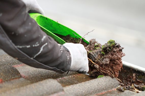 Very dirty gutter being cleared by man with a tool and hand