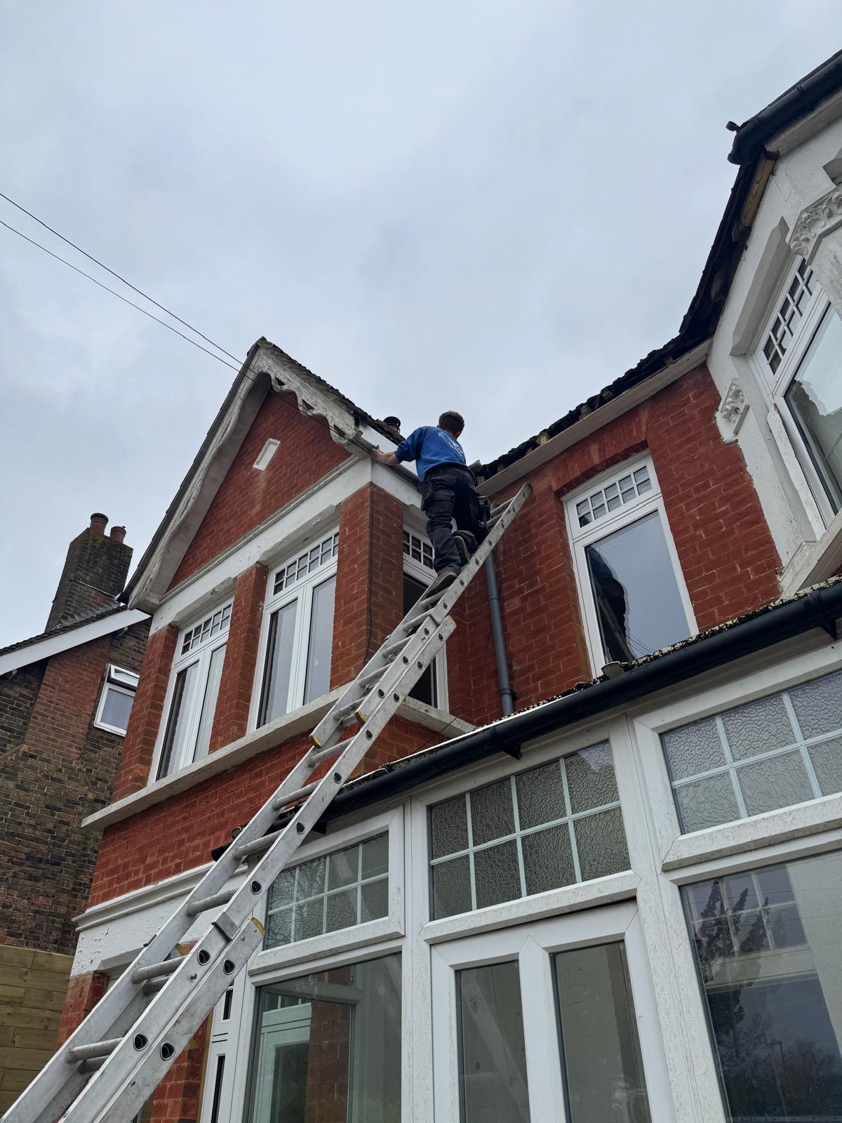 A roofer attaching a white fascia board to a residential property.