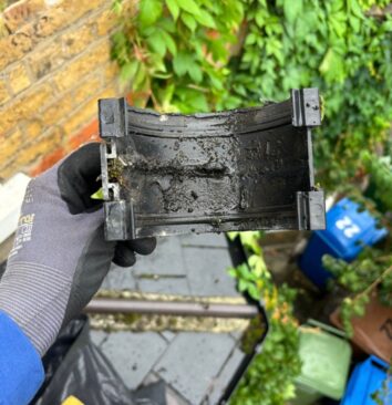 A roofing technician in a black and grey glove holding an old black UPVC gutter union.