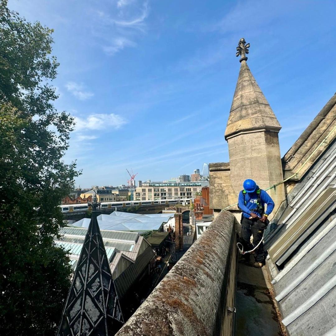 A Sam's Gutters & Roofs roofer fastening his harness on top of a cathedral in London.