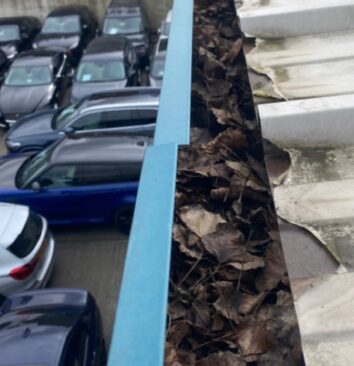 A before photo of a gutter that is full of leaves on an industrial building.