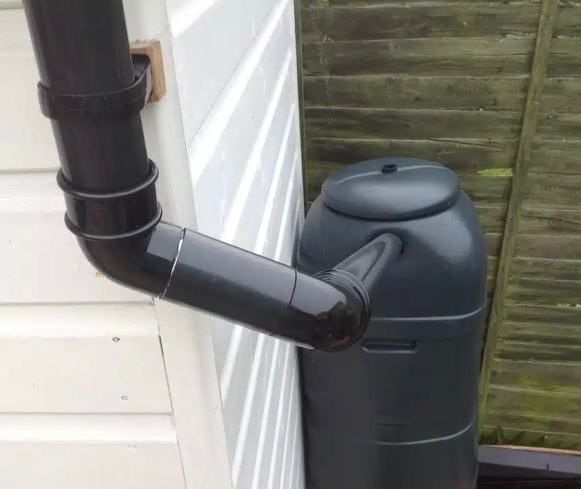A black water butt connected to a black UPVC downpipe.