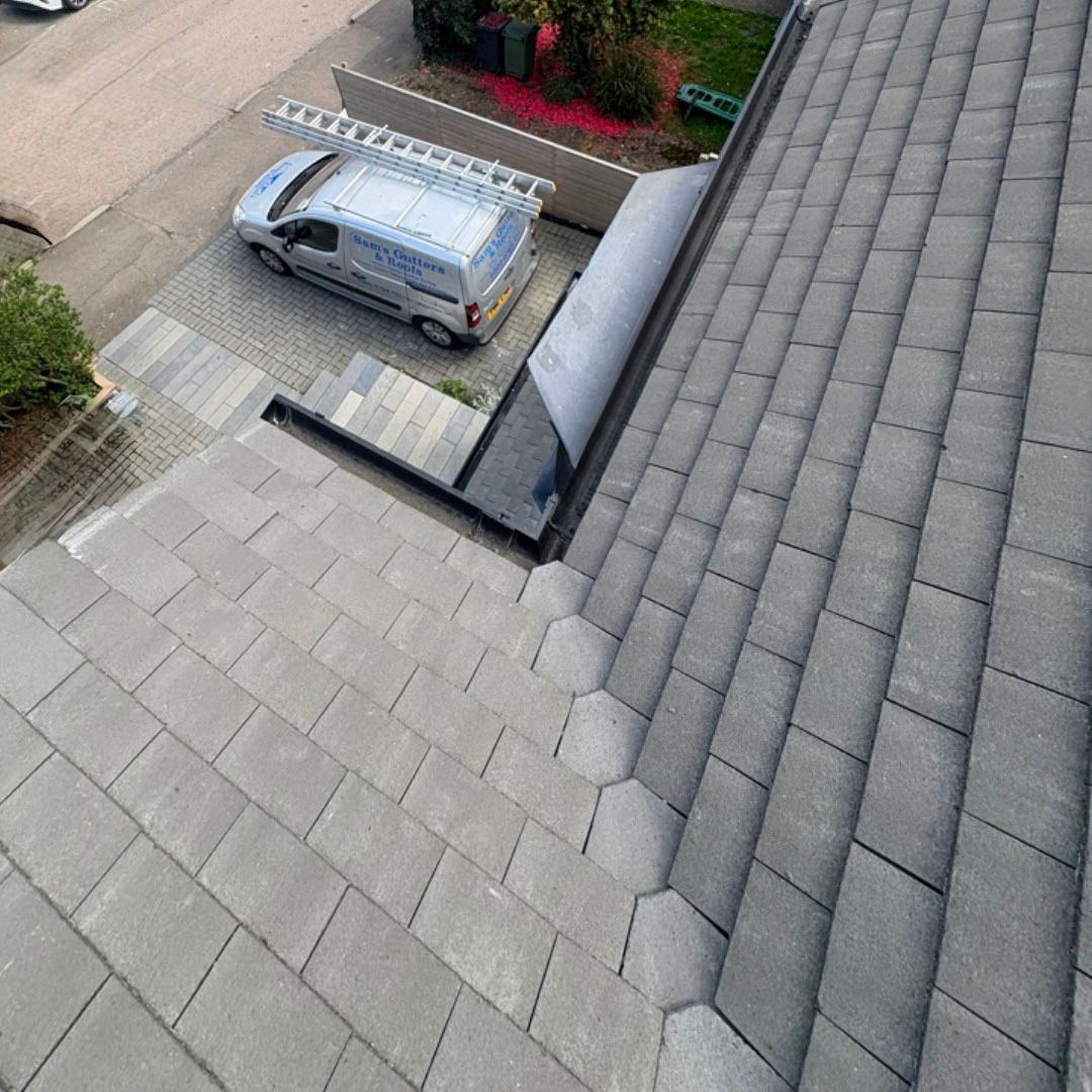 A slate tiled roof with a Sam's Gutters & Roofs company van parked on driveway.