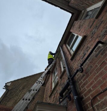 A roofer on the top of a ladder inspecting a white fascia board.