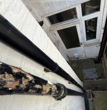 An old black cast iron downpipe next to a new black UPVC downpipe.