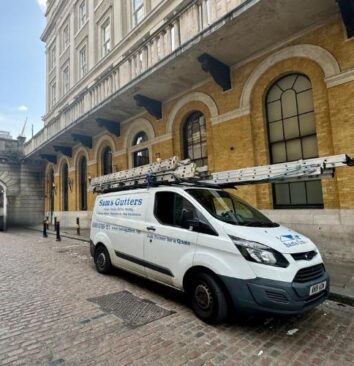 A Sam's Gutters & Roofs van with a long ladder on top sitting outside an office block in London.