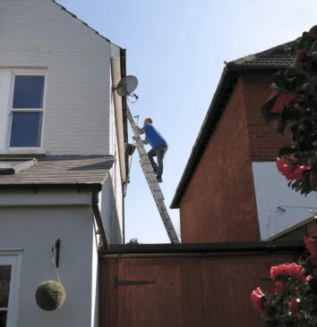 A roofing technician climbing a ladder on a 2 storey property.