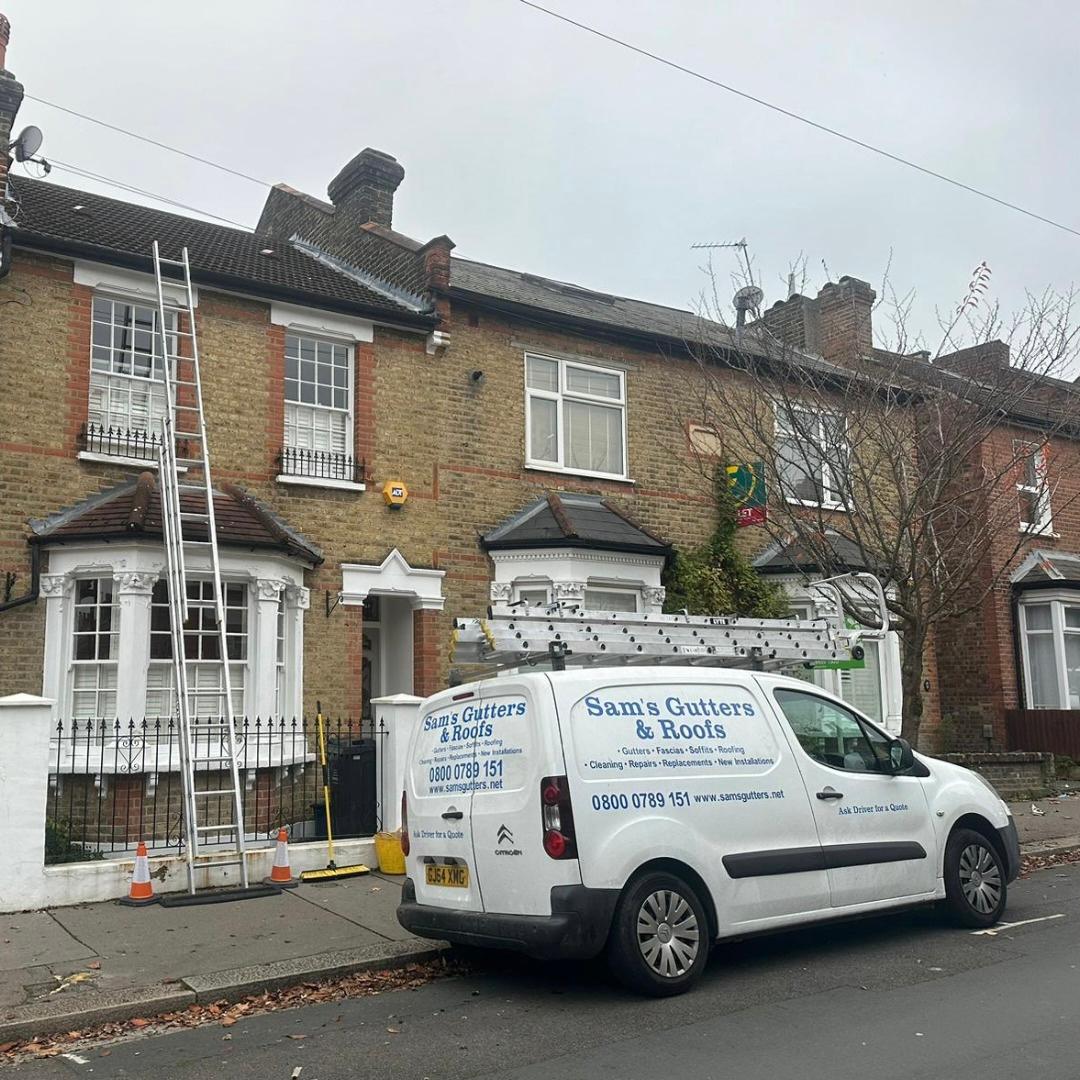 A Sam's Gutters and Roofs van parked outside a residential property with a ladder leaning against the second storey roof line.