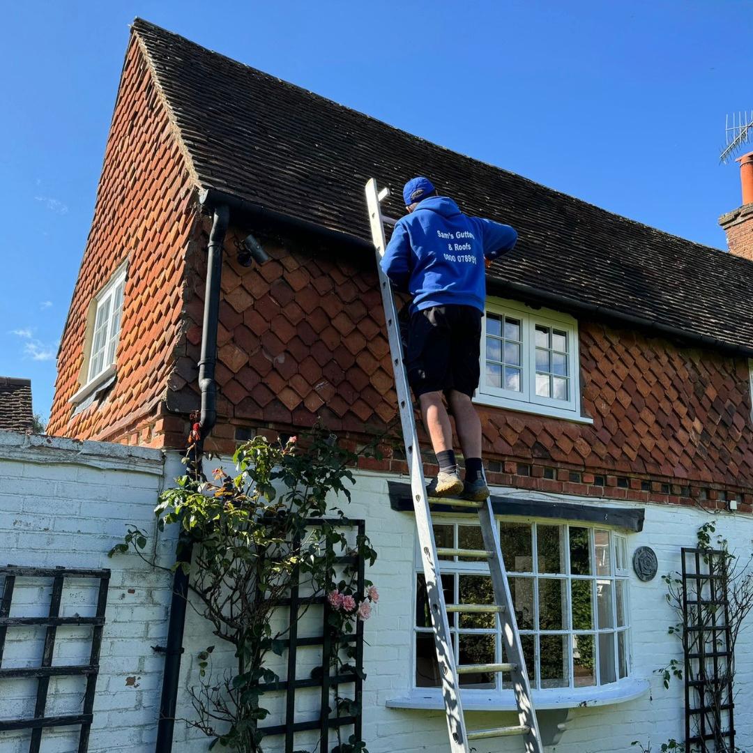 A Sam's Gutters and Roofs technician on the top of a 2 storey ladder leaning on the roof line of a Victorian style property.