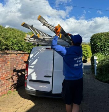 A Sam's Gutters and Roofs roofer taking the ladder off of a white van .